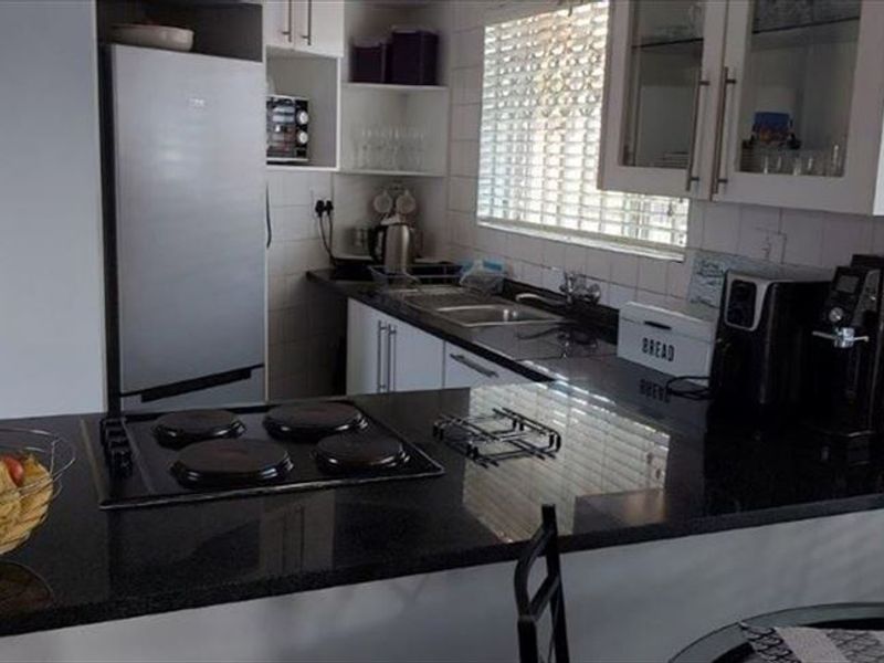 A functional kitchen featuring granite countertops, an electric hob, built-in cabinetry, and a tiled backsplash with natural light from the window.