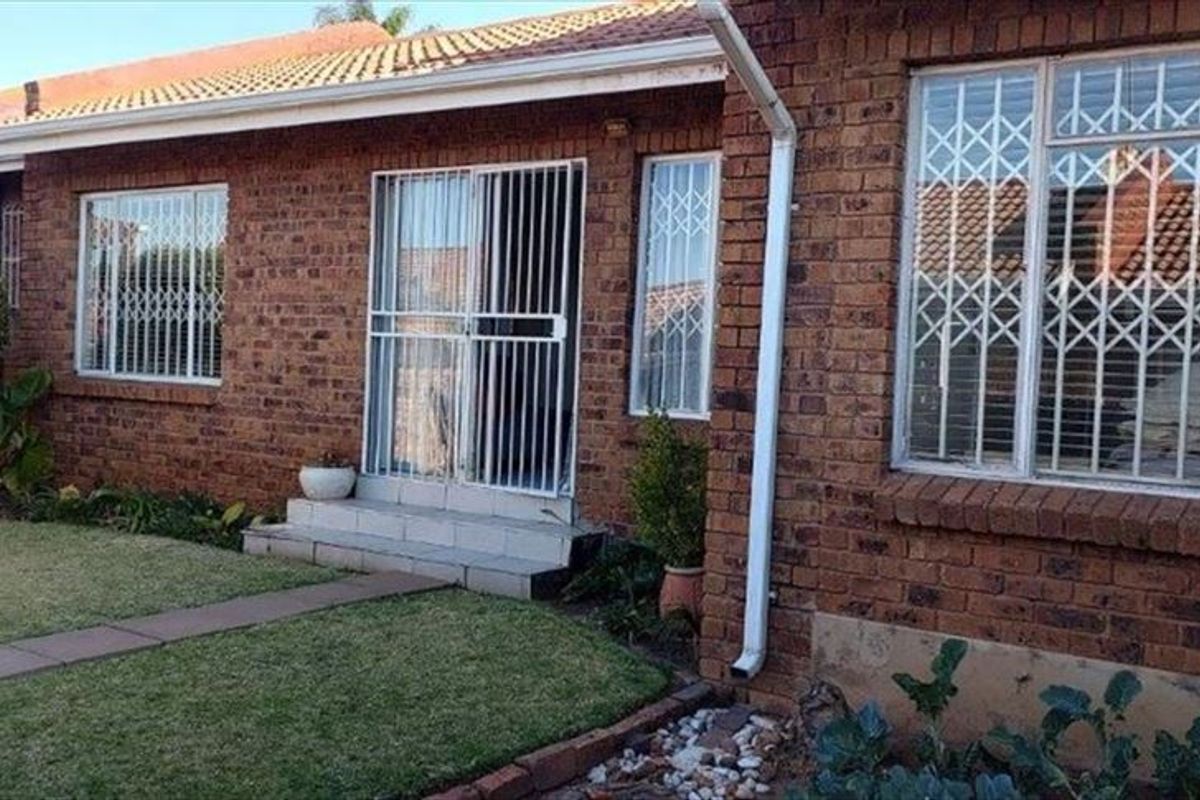Rear view of a face brick townhouse featuring a tiled roof, security-fitted windows and doors, and a small garden with a paved walkway.