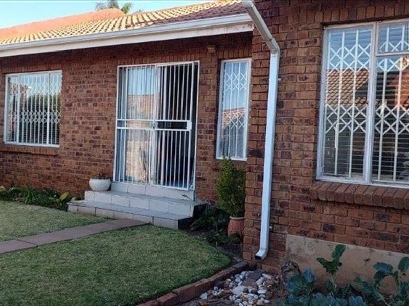 Rear view of a face brick townhouse featuring a tiled roof, security-fitted windows and doors, and a small garden with a paved walkway.