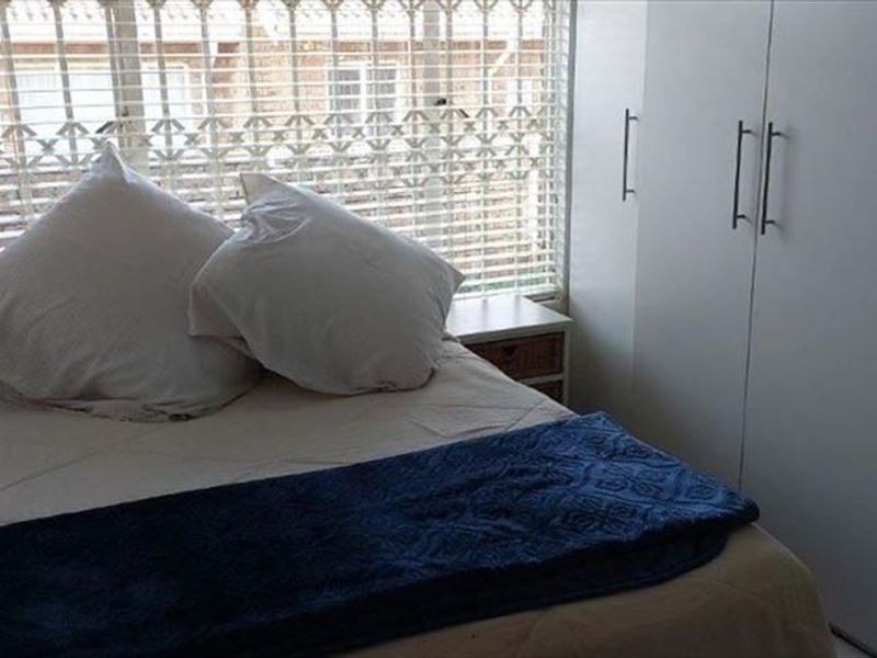 A compact bedroom featuring built-in cupboards, security bars on the window, and venetian blinds, providing a functional and secure living space.