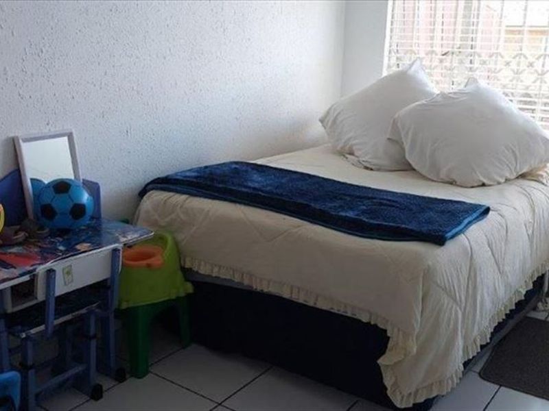 A functional bedroom featuring tiled flooring and a window with a security gate, providing a practical space for rest.