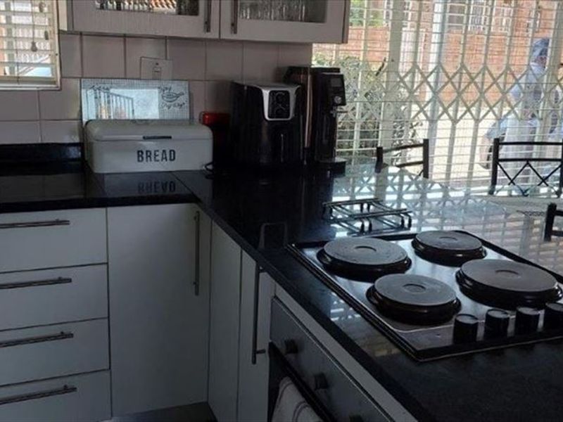 A functional kitchen featuring black granite countertops, white cabinetry, an electric hob, and a built-in oven, with direct access to an outdoor area.