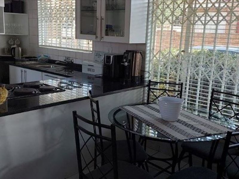Open plan kitchen and dining area featuring granite countertops, built-in cabinetry, and tiled flooring, with direct access to a secure exterior area.