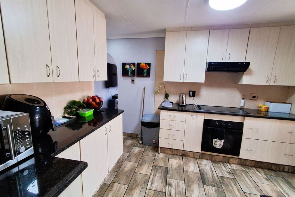 Functional kitchen featuring light-toned cabinetry, dark granite countertops, integrated oven, hob, and extractor fan with wood-look tiled flooring.