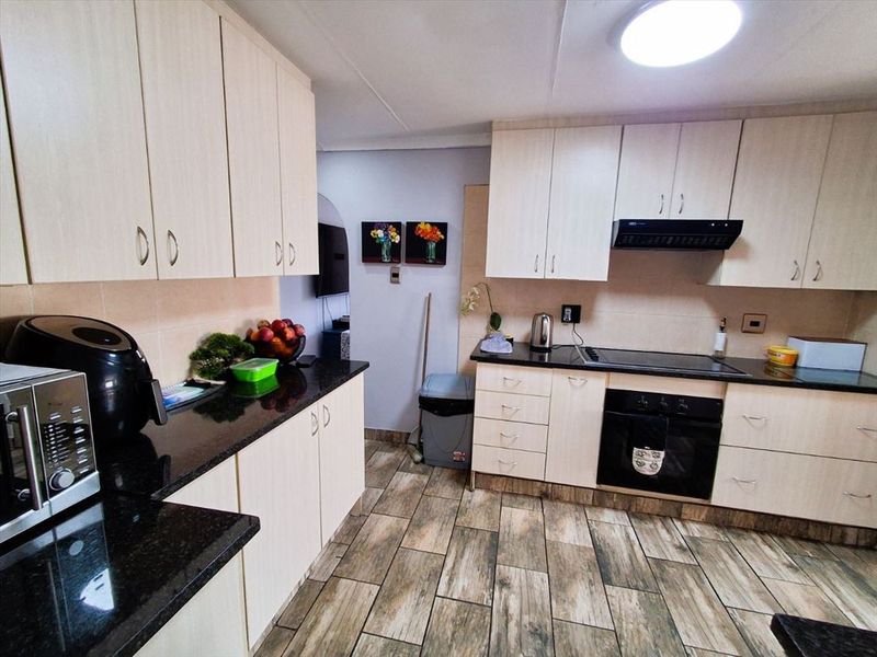 Functional kitchen featuring light-toned cabinetry, dark granite countertops, integrated oven, hob, and extractor fan with wood-look tiled flooring.