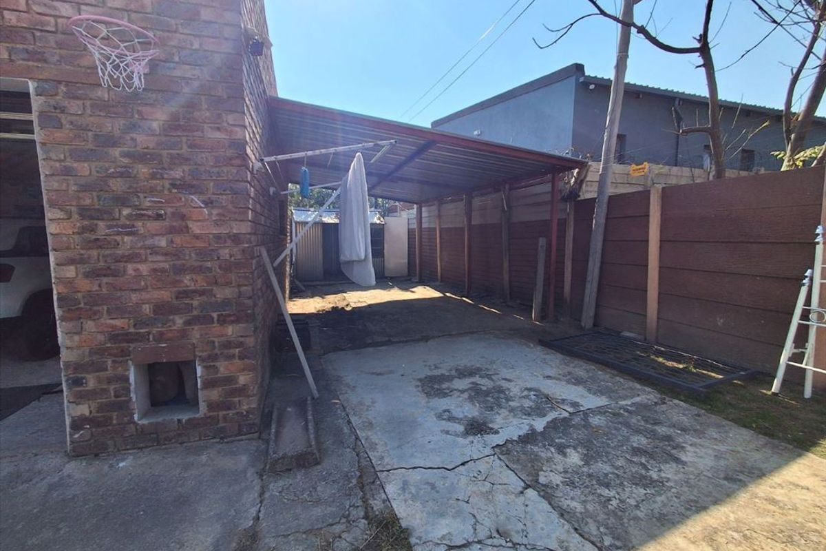 Rear exterior area featuring a brick facade, a metal carport structure, and a concrete driveway with visible surface cracking.