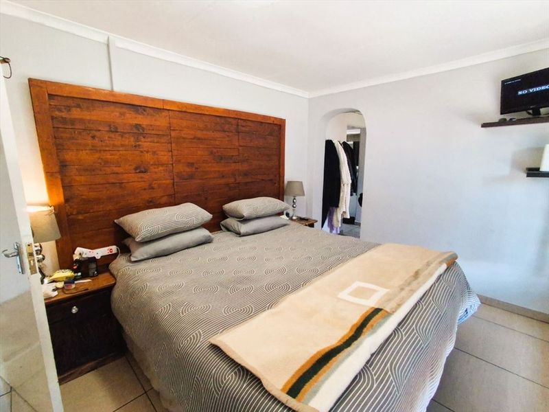 A bedroom featuring a large wooden headboard, tiled flooring, and an arched doorway leading to an adjoining space.