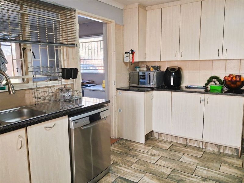 Functional kitchen featuring light wood-finish cabinetry, granite countertops, tiled flooring, and a stainless steel sink with a view into the adjacent utility area.
