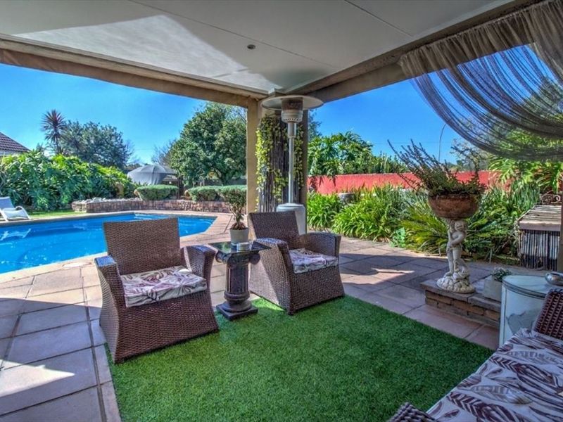A covered outdoor patio area featuring paved flooring, overlooking a private swimming pool and landscaped garden.