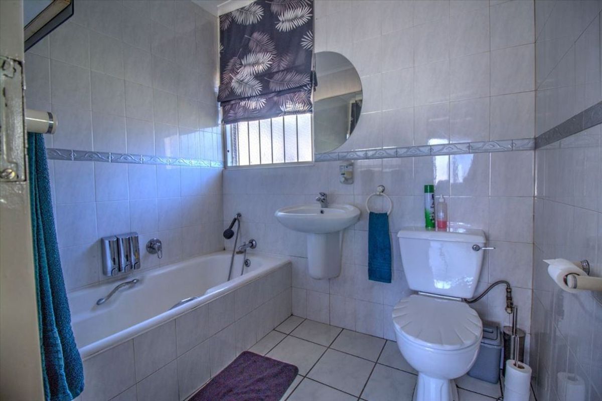 A functional bathroom featuring a pedestal basin, bathtub, and toilet with neutral wall and floor tiling.