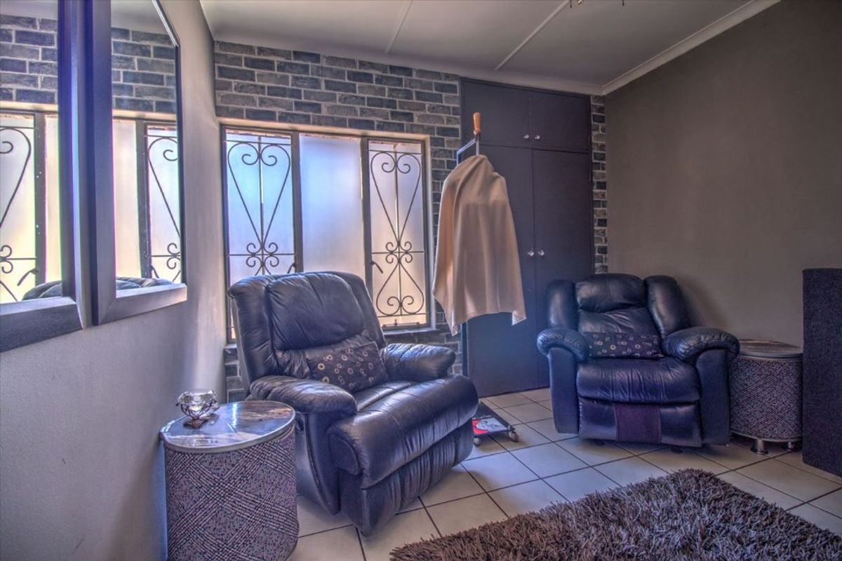 A bedroom featuring tiled flooring, an exposed brick accent wall, and built-in cupboards with security bars on the windows.
