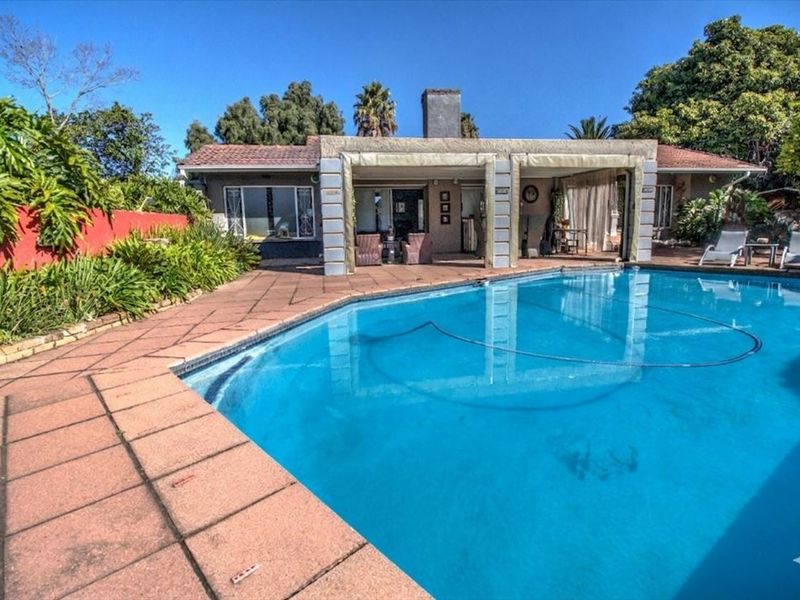 Outdoor pool area featuring a large swimming pool, paved deck, and a covered patio space with a prominent chimney stack.