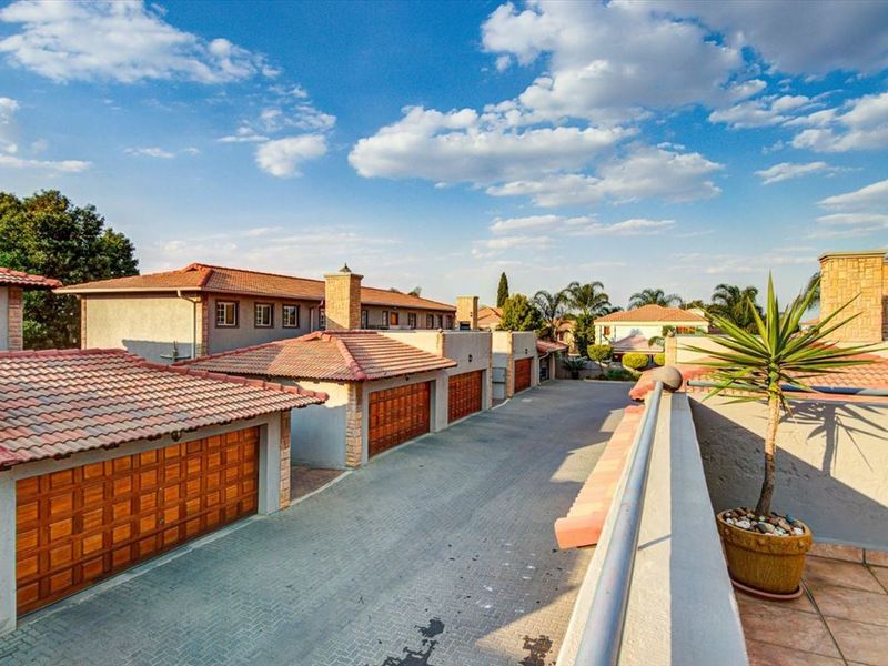 An elevated view of a townhouse complex driveway featuring multiple garages with wooden doors, tiled roofs, and stone-clad architectural details.