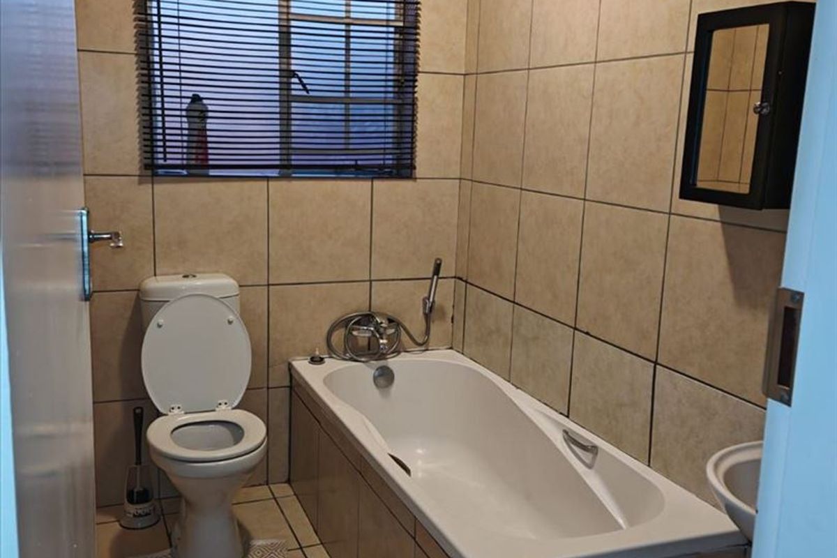 A functional bathroom featuring tiled walls and flooring, a standard bathtub, a toilet, and a wall-mounted storage cabinet.