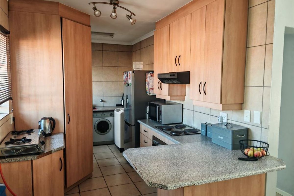 A functional kitchen featuring laminate cabinetry, granite countertops, an electric hob, and integrated laundry space with tiled flooring and backsplash.