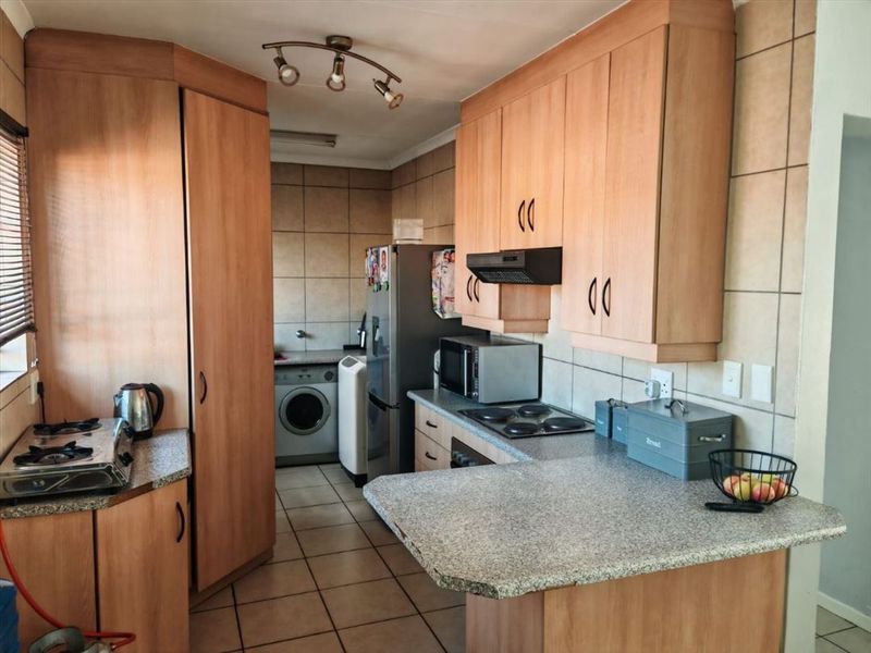A functional kitchen featuring laminate cabinetry, granite countertops, an electric hob, and integrated laundry space with tiled flooring and backsplash.