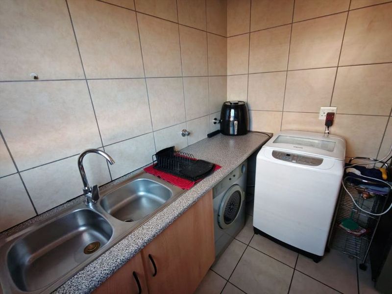 A functional laundry area featuring a double stainless steel sink, laminate countertop, tiled splashback, and dedicated plumbing connections for laundry appliances.