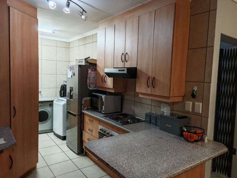 A functional kitchen featuring laminate cabinetry, granite countertops, built-in oven, electric hob, and tiled finishes throughout.