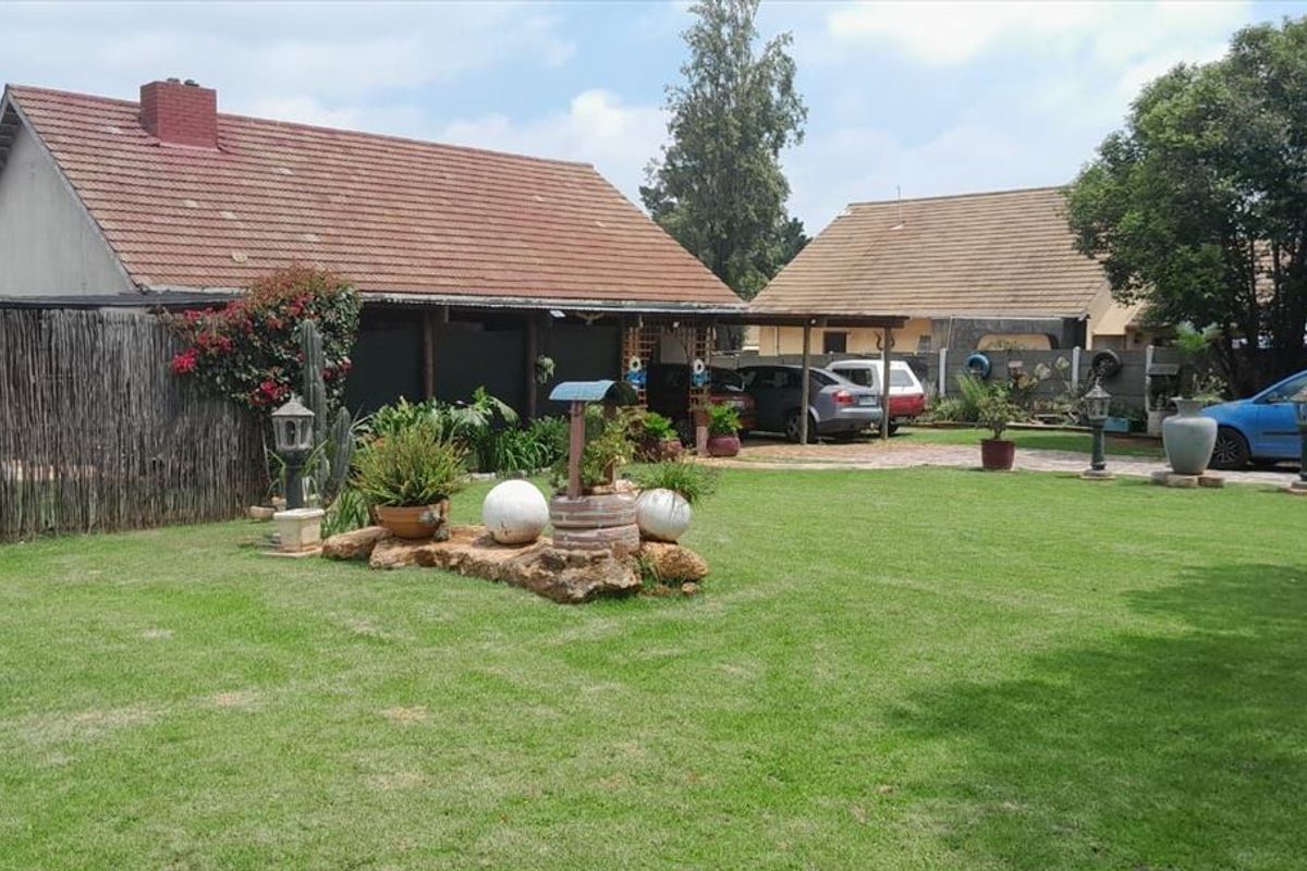 A spacious rear garden featuring a well-maintained lawn, paved driveway, and a covered carport area adjacent to the main house structure.
