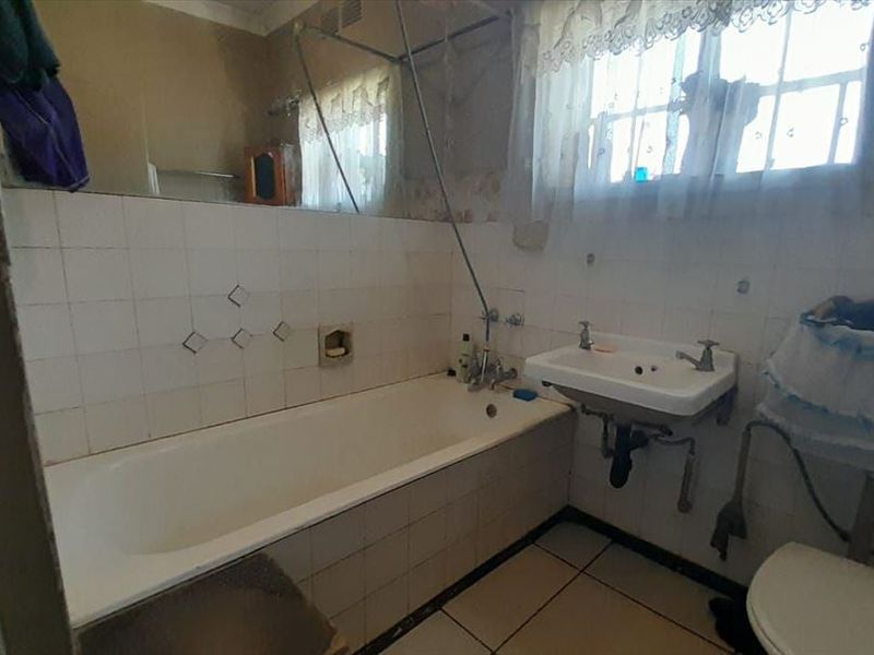 A dated bathroom featuring a built-in bathtub, wall-mounted basin, and tiled finishes, offering potential for a modern renovation.