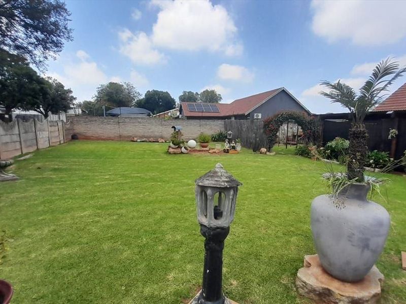 A spacious rear garden featuring a well-maintained lawn, enclosed by precast concrete boundary walls, with a view of the main house roof and solar panels.