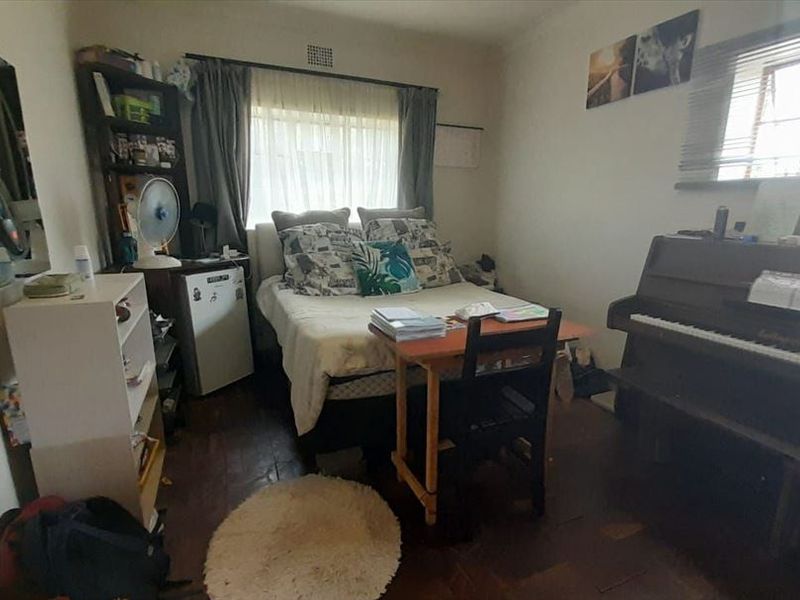 A bedroom featuring parquet flooring and natural light through a window, offering a functional space for rest or study.