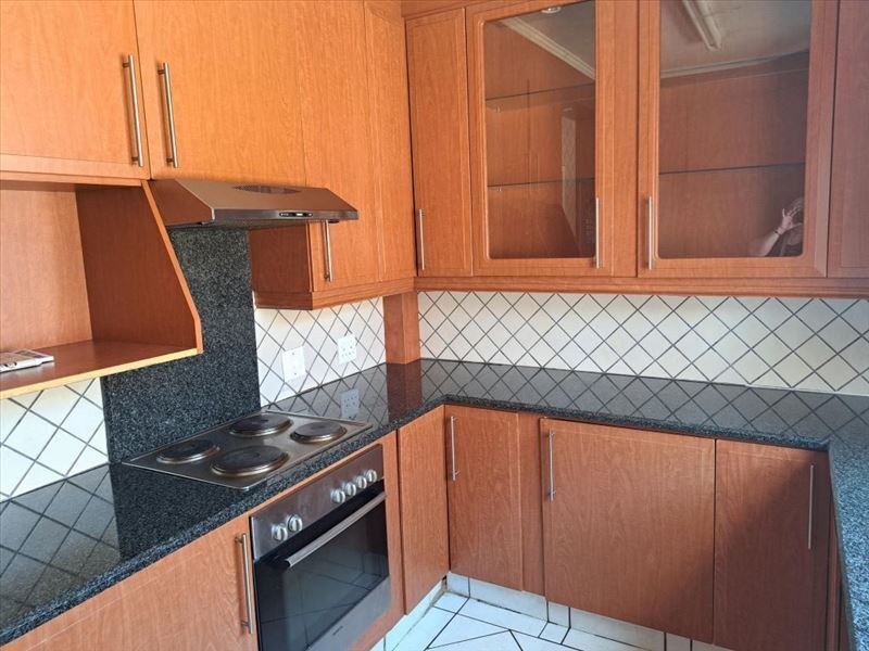 A functional kitchen featuring wood-look laminate cabinetry, granite countertops, a built-in oven, and an electric hob with a tiled backsplash.