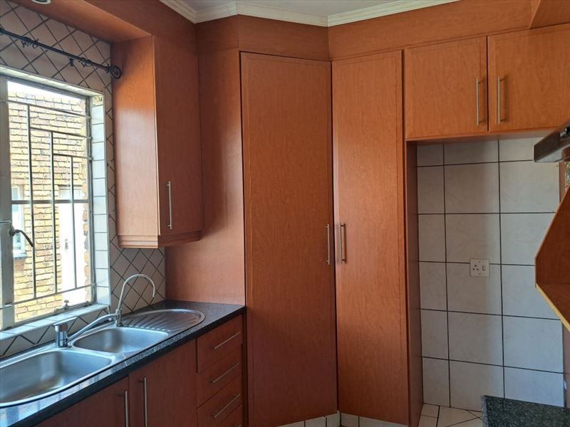 A functional kitchen featuring wood-look laminate cabinetry, a double stainless steel sink, and tiled splashbacks, offering a clean and practical workspace.