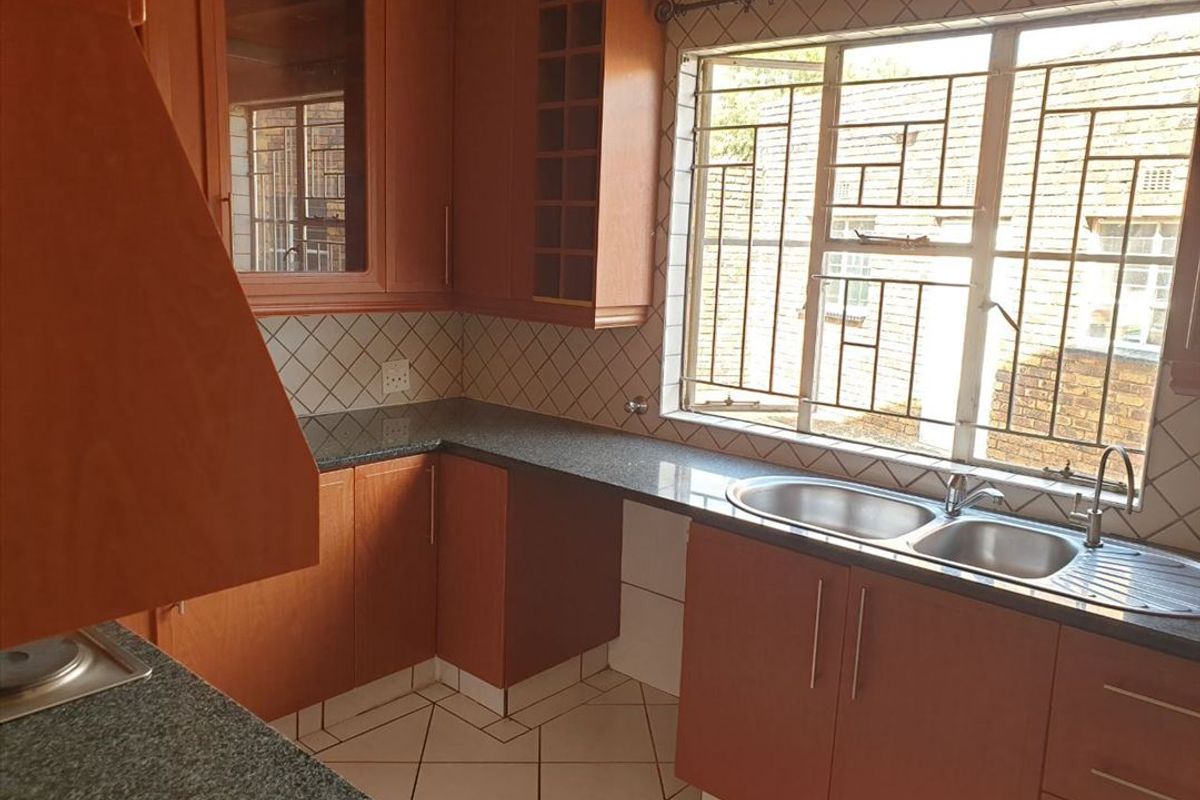 A functional kitchen featuring wood-finish cabinetry, granite countertops, a double bowl sink, and tiled flooring, offering a clean and practical workspace.