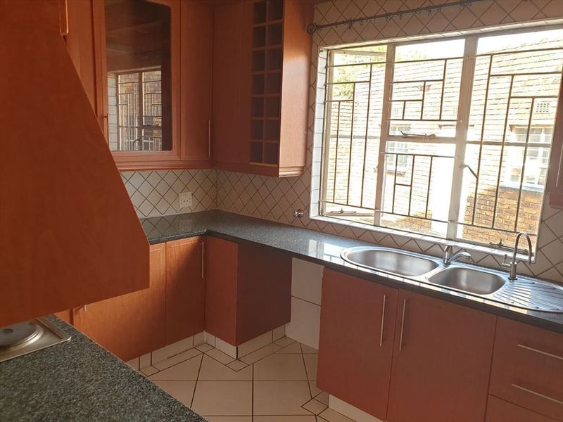 A functional kitchen featuring wood-finish cabinetry, granite countertops, a double bowl sink, and tiled flooring, offering a clean and practical workspace.