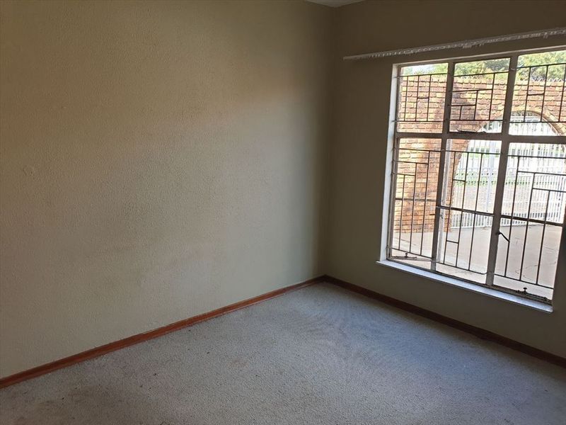 An empty bedroom featuring carpet flooring and a large window fitted with security bars, offering a blank canvas for potential updates.