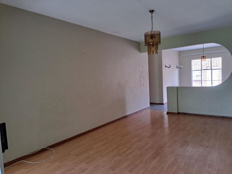 An empty living room featuring laminate flooring, a distinctive architectural archway, and vintage pendant lighting, offering a blank canvas for interior design.