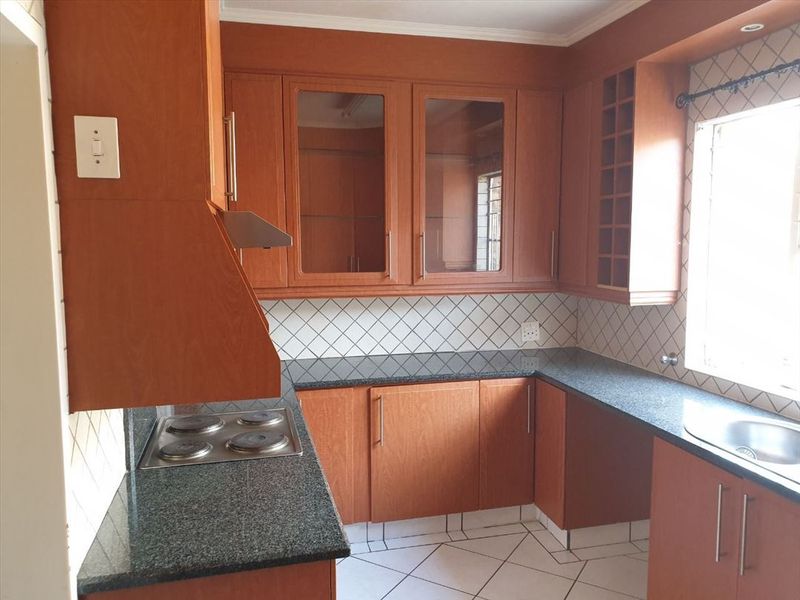 A functional kitchen featuring wood-finish cabinetry, granite countertops, a built-in electric hob with extractor, and tiled flooring.