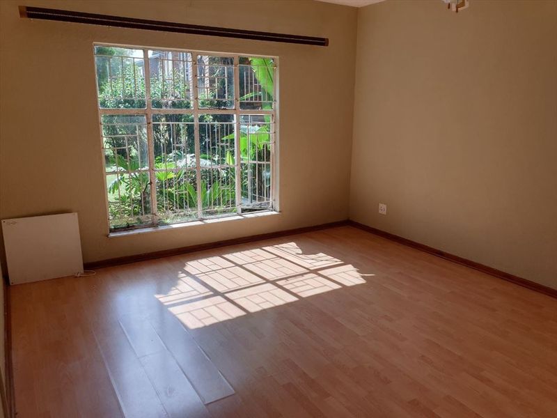 An empty bedroom featuring laminate flooring, large windows with security bars, and neutral wall tones, offering a blank canvas for personalization.