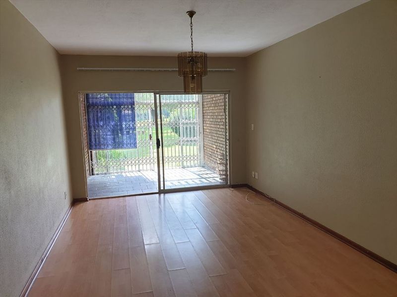 An empty living room featuring laminate flooring and a sliding glass door with a security gate leading to an outdoor area.