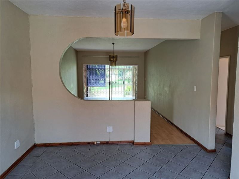 Open plan living area featuring a distinctive architectural archway, mixed tile and laminate flooring, and access to an outdoor space through a security gate.