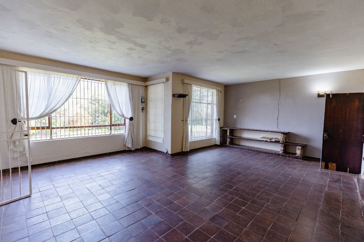 Spacious living area featuring tiled flooring, security bars on windows, and built-in shelving, offering a blank canvas for renovation.