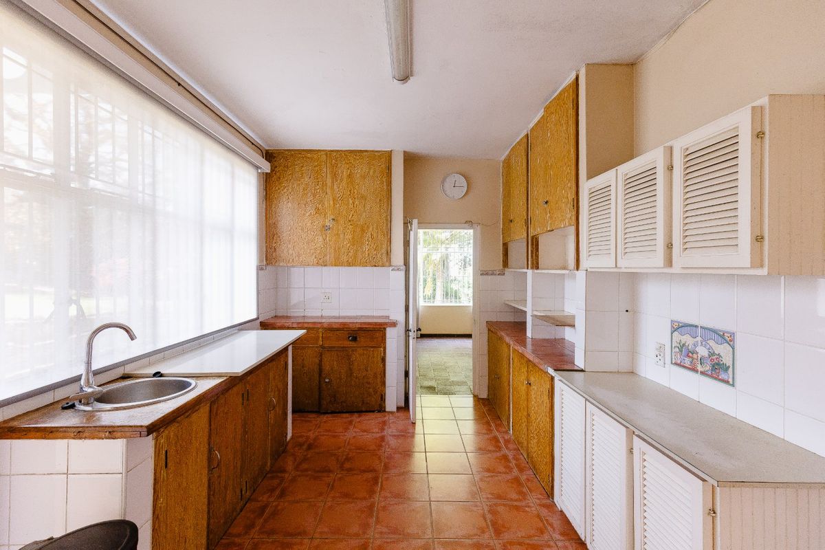 A dated kitchen featuring original wooden cabinetry, tiled countertops, and ceramic flooring, offering a functional layout ready for modern renovation and updates.