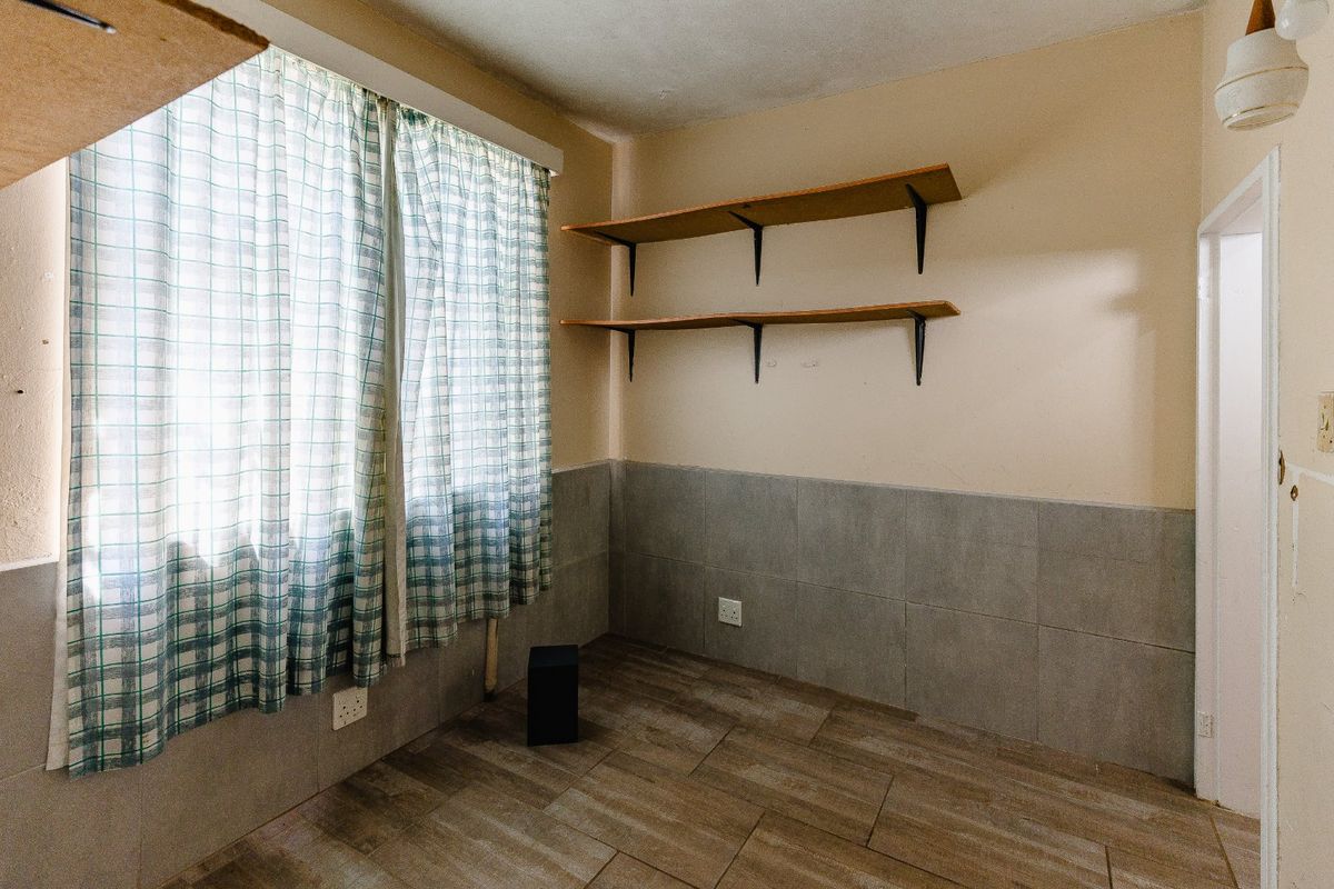 A simple, empty bedroom featuring tiled flooring, wall-mounted shelving, and partial wall tiling, offering a blank canvas for potential renovation or restyling.