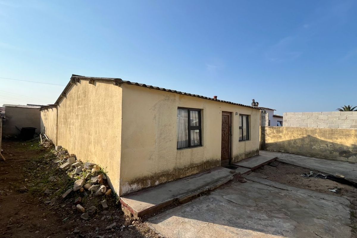 Rear view of a detached house featuring a concrete apron, perimeter boundary walls, and corrugated roof sheeting, showing signs of exterior wear.