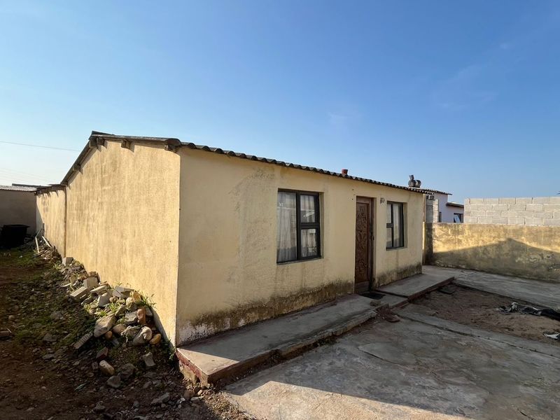 Rear view of a detached house featuring a concrete apron, perimeter boundary walls, and corrugated roof sheeting, showing signs of exterior wear.