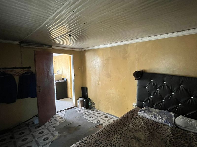 A bedroom featuring tiled flooring and a corrugated ceiling, currently showing significant wear and requiring cosmetic updates to improve the overall condition.