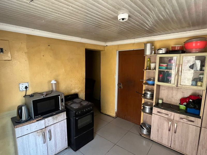 A dated kitchen area featuring basic cabinetry, a freestanding stove, and tiled flooring, requiring cosmetic updates to improve the overall aesthetic and functionality.