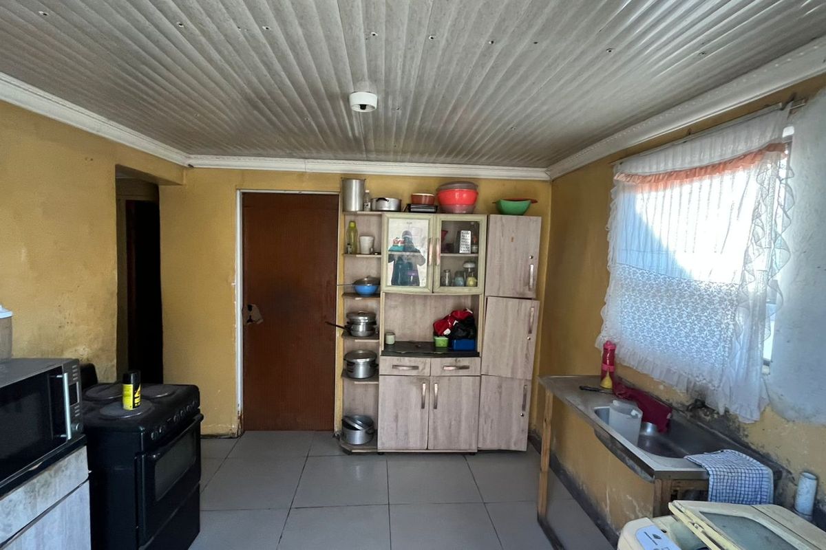 A functional kitchen space featuring tiled floors, built-in cabinetry, a stainless steel sink, and a freestanding stove, requiring cosmetic updates and wall repairs.