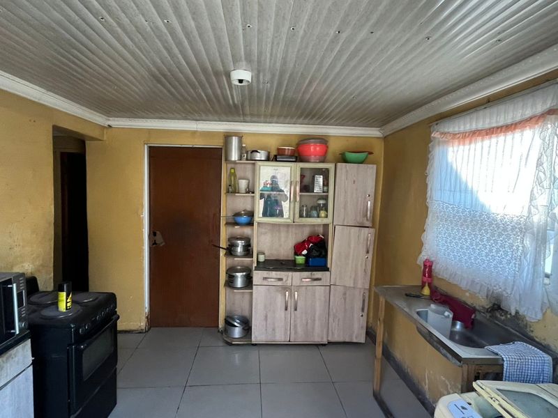 A functional kitchen space featuring tiled floors, built-in cabinetry, a stainless steel sink, and a freestanding stove, requiring cosmetic updates and wall repairs.
