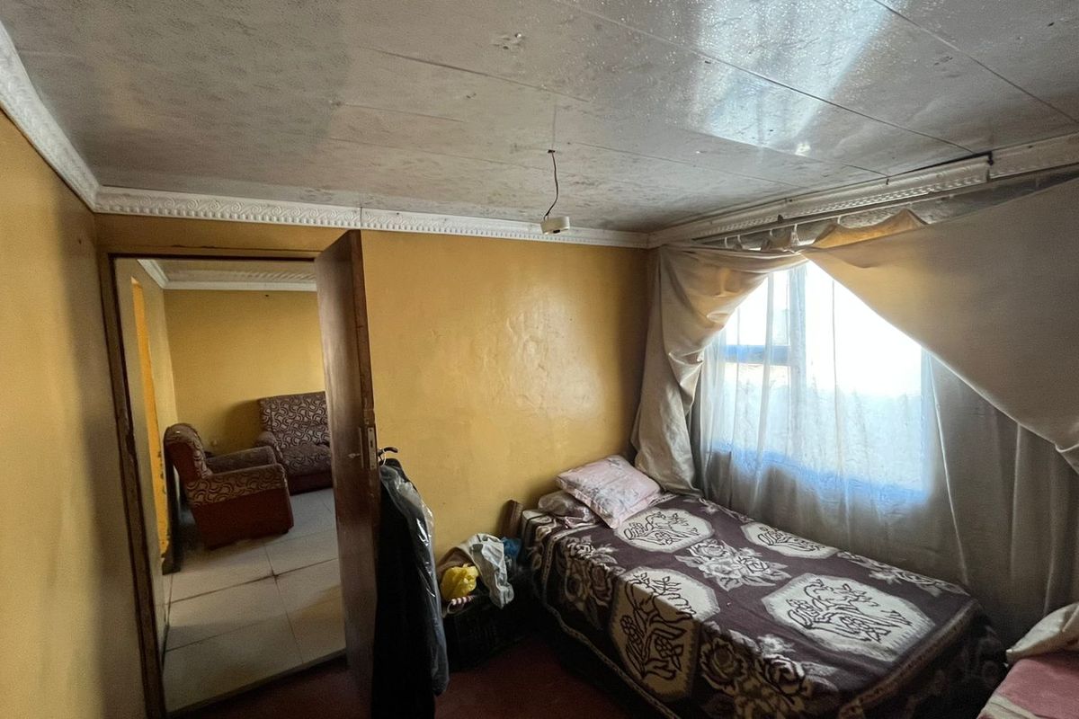 A bedroom featuring a tiled ceiling with decorative cornice and a window, currently showing signs of wear and requiring cosmetic updates.