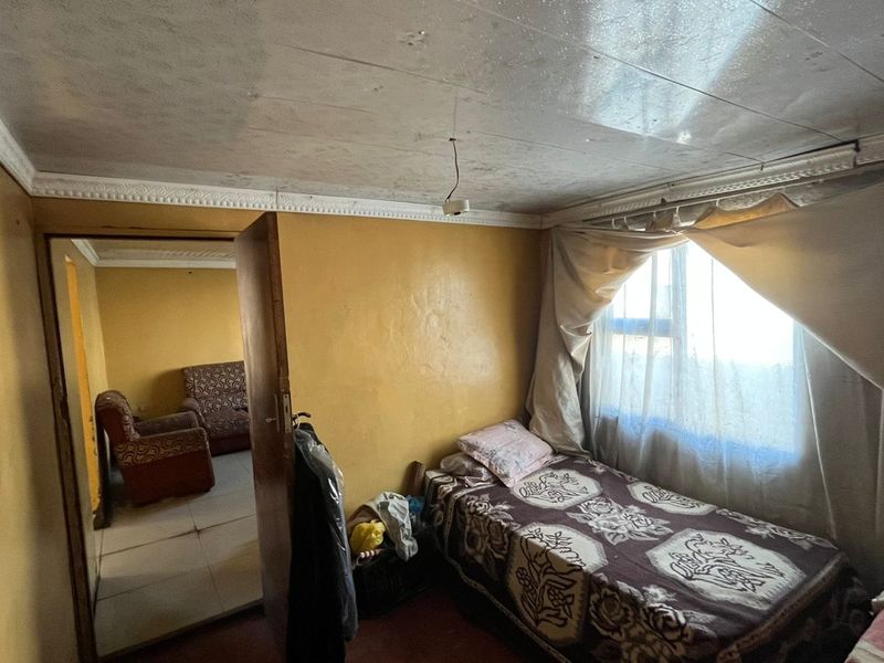 A bedroom featuring a tiled ceiling with decorative cornice and a window, currently showing signs of wear and requiring cosmetic updates.