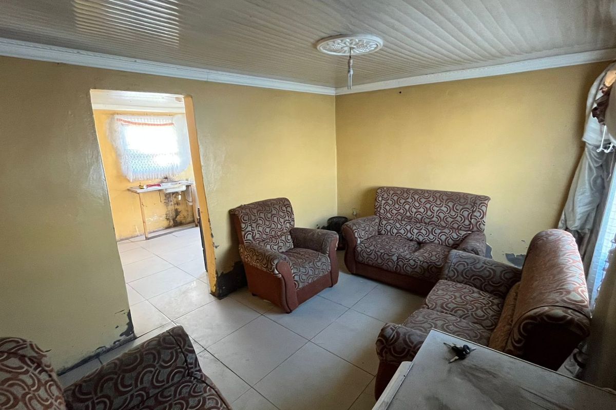 A living room area featuring tiled flooring and decorative ceiling details, requiring cosmetic updates and wall repairs to improve the overall condition.