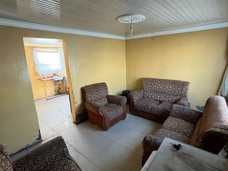 A living room area featuring tiled flooring and decorative ceiling details, requiring cosmetic updates and wall repairs to improve the overall condition.