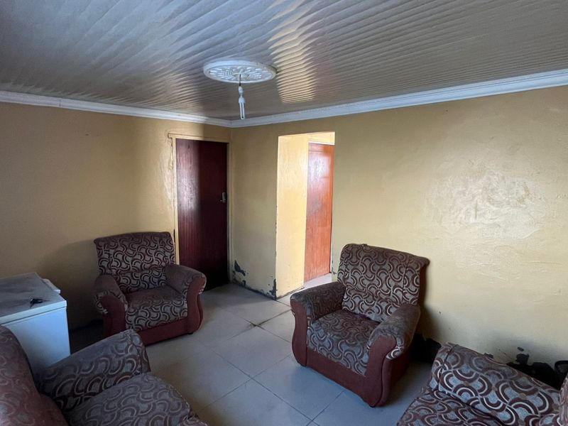 A living room area featuring tiled flooring, coving, and a ceiling rose, currently requiring cosmetic updates and wall repairs.